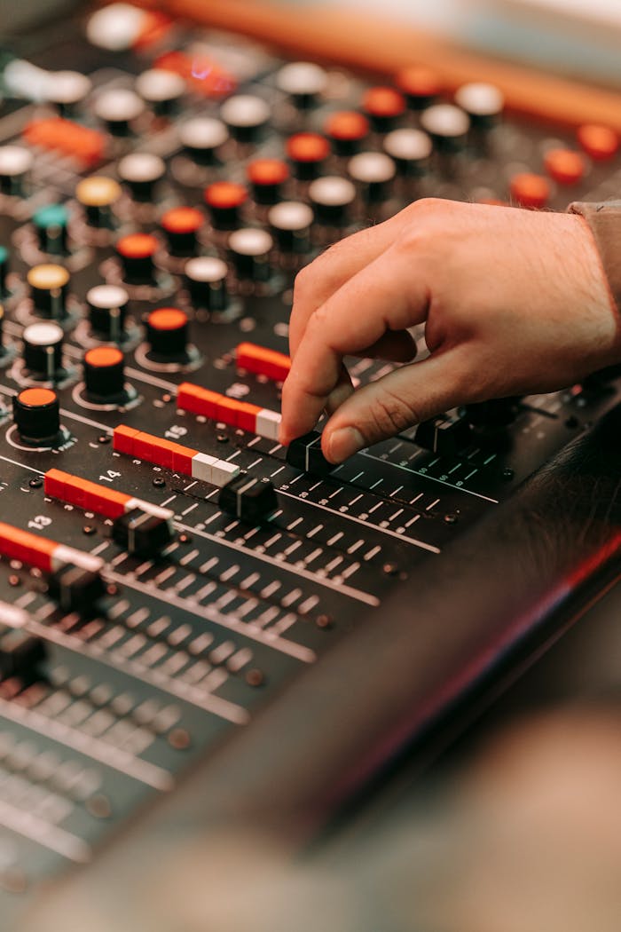 A detailed close-up of a hand adjusting knobs and sliders on an audio mixer in a studio setting.